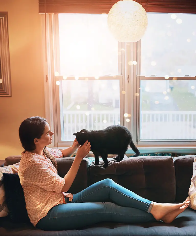 Eine Frau sitzt auf der Couch mit ihrer Katze, die durch eine Krankenversicherung sinnvoll abgesichert ist.